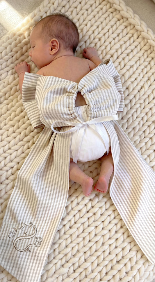 Back view of newborn baby wearing personalized name sash with oversized bow and tie closure, neutral striped fabric