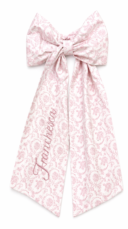 Personalized pink floral newborn name sash bow with embroidered script name detail for baby girl hospital announcement photos and luxury coming home styling.