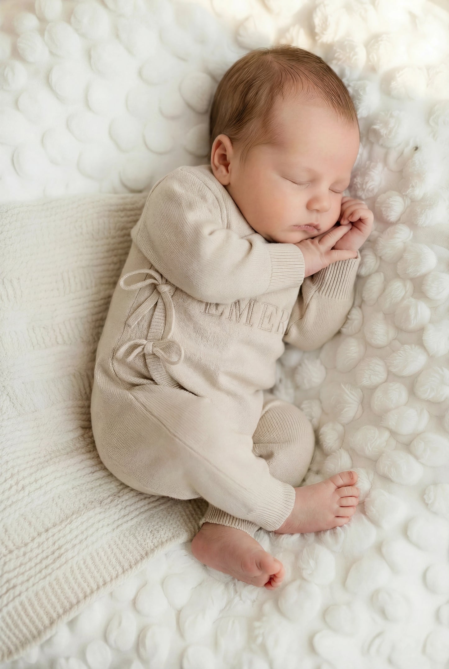 Newborn baby wearing classic knit wrap romper in soft khaki, lying on textured knit blanket