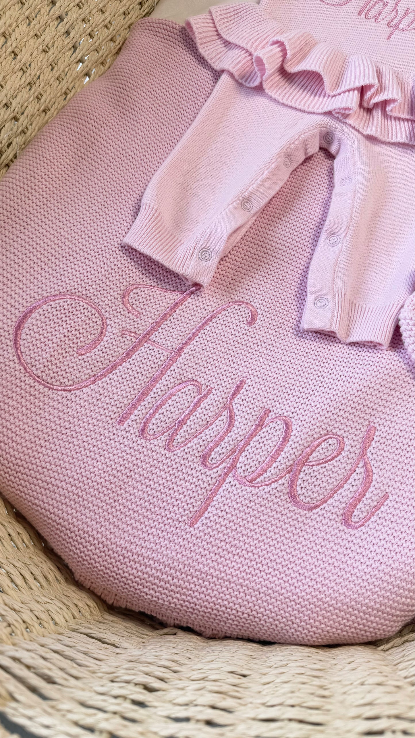 Close-up of a petal pink ruffle knit blanket embroidered with the name Harper and matching newborn accessories.