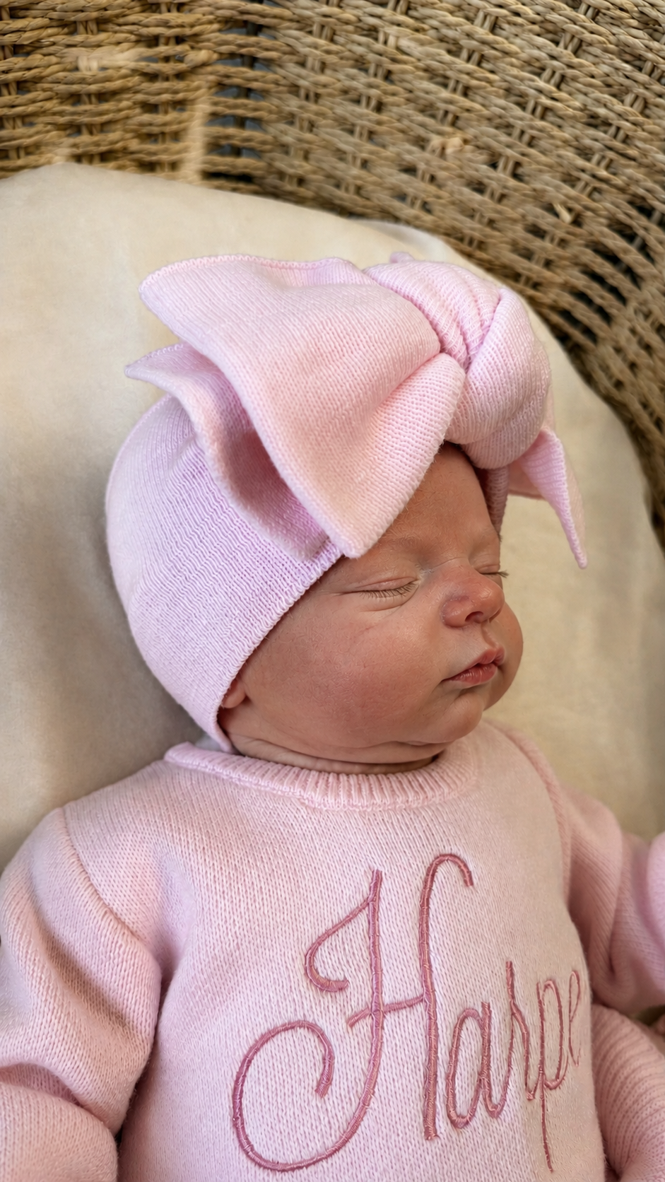 Close-up of a newborn wearing an oversized petal pink bow headwrap and personalized Ballerina knit romper.