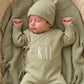 Newborn wearing a personalized Soft Sage kimono romper with matching bear-ear hat and knit booties on a coordinating knit blanket.