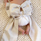 Back view of newborn baby wearing personalized name sash with oversized bow and tie closure, neutral striped fabric