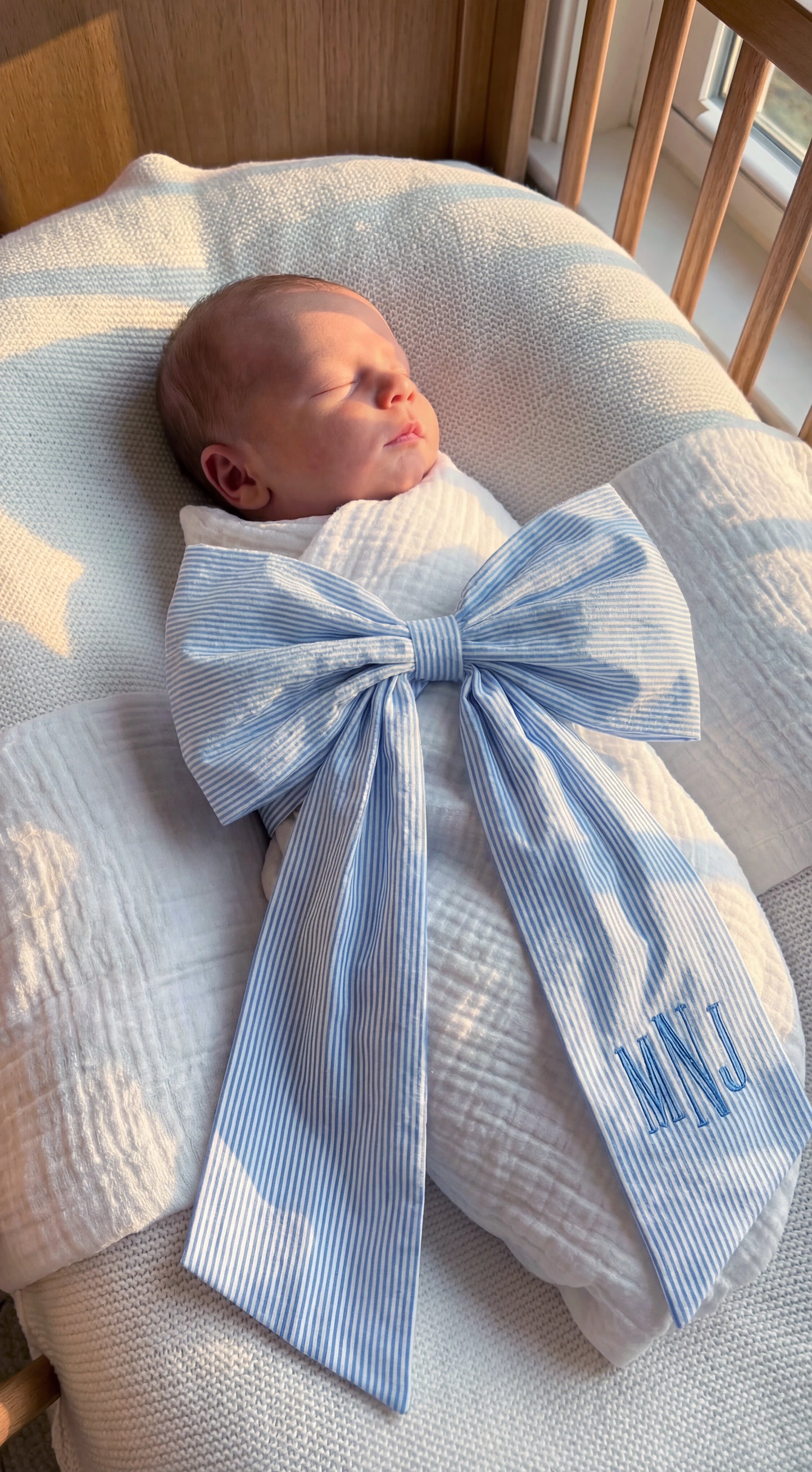 Newborn baby wearing personalized blue striped name sash with oversized bow and embroidered monogram, soft cotton hospital announcement outfit keepsake gift for baby boy