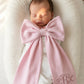 Newborn baby wearing personalized pink name sash with oversized bow and embroidered monogram, soft cotton baby hospital announcement outfit keepsake gift