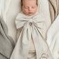 Newborn baby wearing personalized name sash with oversized bow, neutral striped fabric for hospital announcement photo
