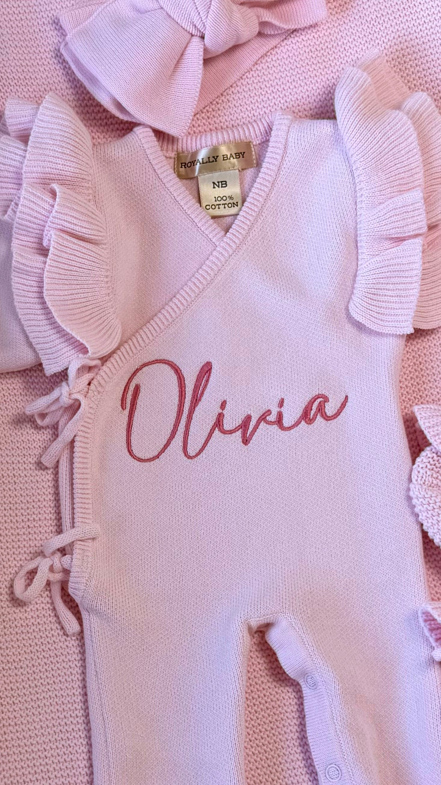 Close-up of personalized name embroidery and butterfly ruffle wrap detailing on a petal pink newborn romper.