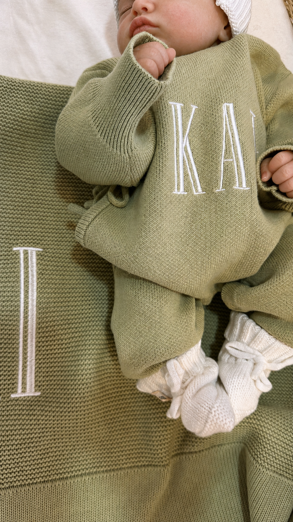 Close-up of name embroidery on a Soft Sage newborn knit romper with a matching blanket and Warm White booties.