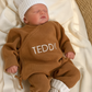 Newborn wearing a personalized Teddy Brown Classic Knit Romper with a coordinating knit hat and booties