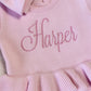 Close-up of Harper name embroidery and layered waist ruffle on the petal pink Ballerina long romper.
