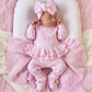 Newborn wearing a personalized petal pink Ballerina long romper with bow headwrap, resting on a matching ruffle knit blanket.
