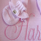 Petal pink ruffle newborn bootie displayed on a personalized knit blanket embroidered with the name Harper.