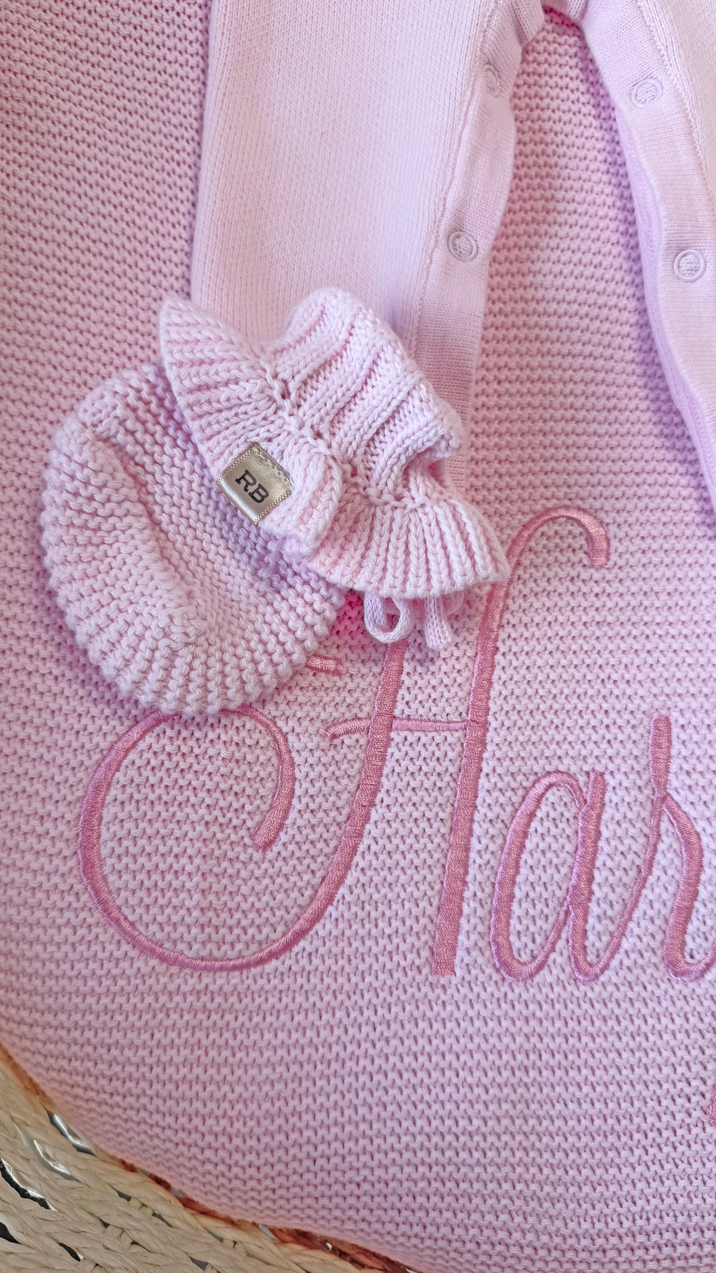 Petal pink ruffle newborn bootie displayed on a personalized knit blanket embroidered with the name Harper.