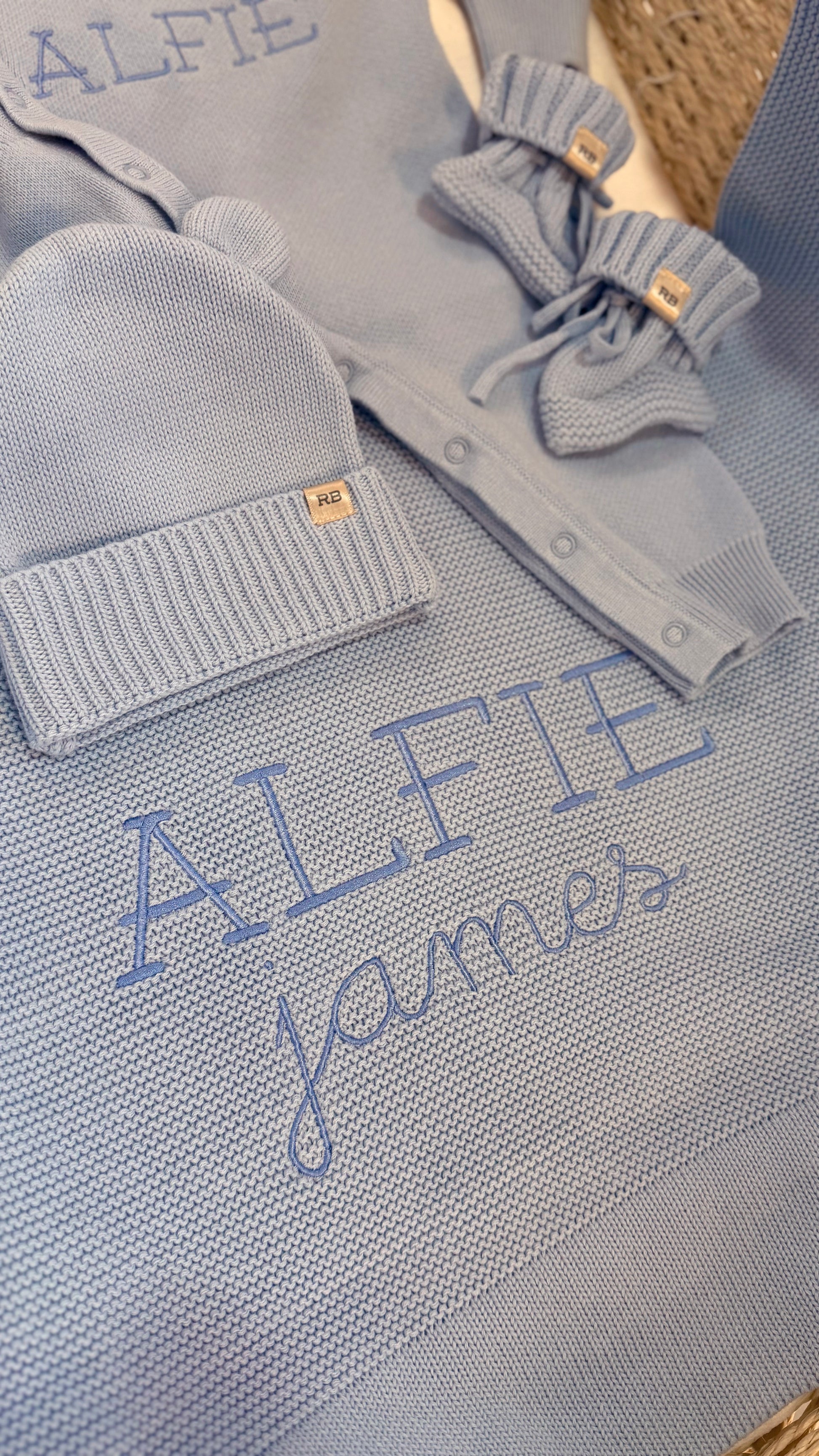 Close-up of the personalized Baby Blue Classic Knit romper and matching blanket embroidered with the name Alfie James.