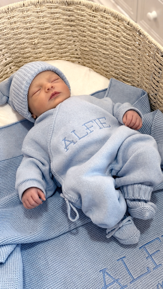 Sleeping newborn wearing the personalized Baby Blue Classic Knit long romper with matching knit hat and booties on an Alfie embroidered blanket.