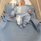 Sleeping newborn wearing the personalized Baby Blue Classic Knit long romper set in a woven bassinet with a matching Alfie blanket.