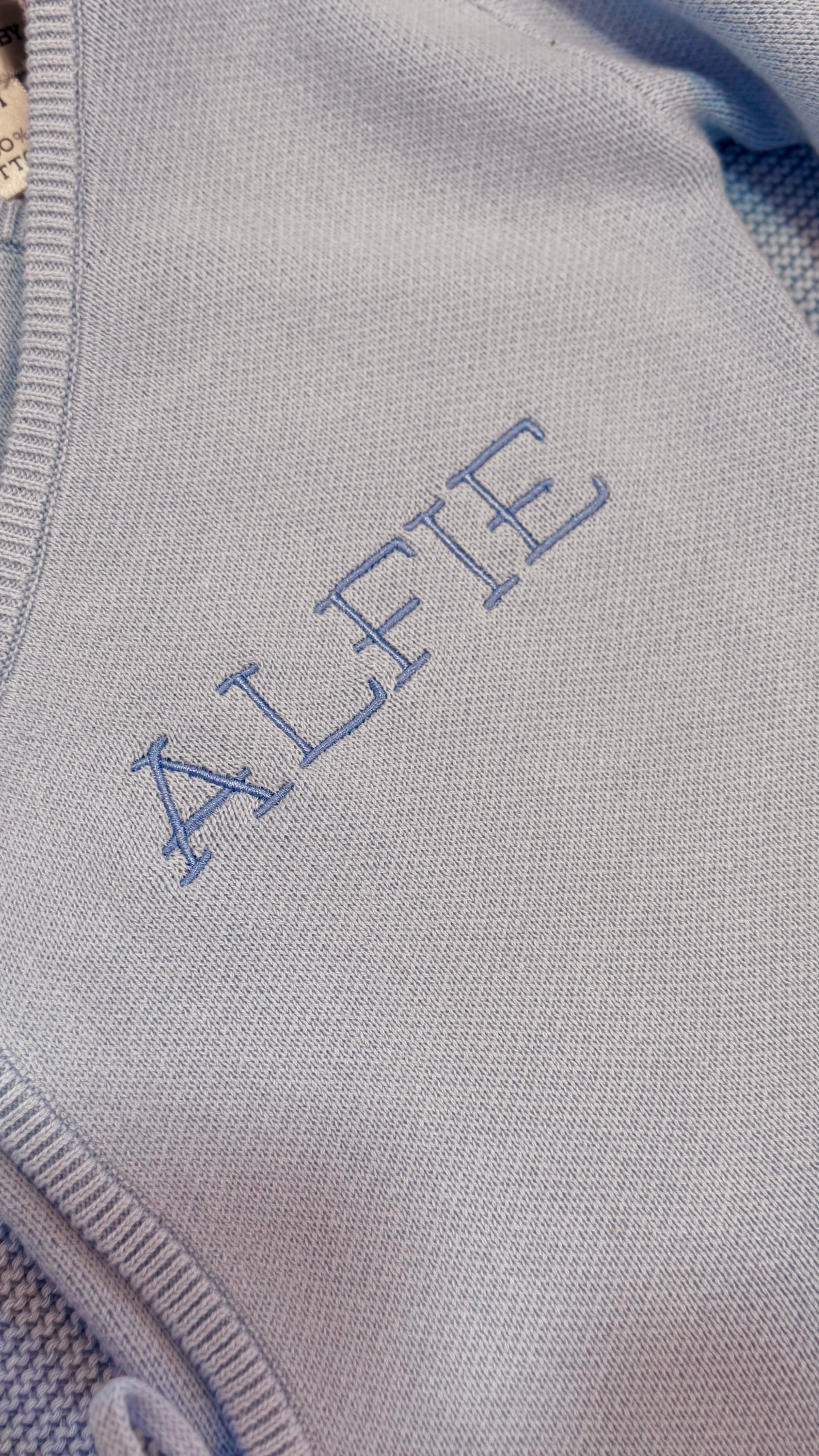 Close-up of Alfie name embroidery on the Baby Blue Classic Knit long newborn romper.