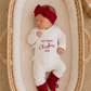 Newborn girl wearing a personalized Christmas romper embroidered My First Christmas with a matching bow
