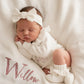 Newborn baby wearing soft ivory wrap romper set with bow and booties on personalized knit blanket