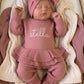 Overhead view of a newborn wearing the personalized Dusty Mauve Ballerina long romper set with matching bow and ruffle booties.