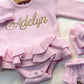 Personalized pink ballerina knit baby romper with ruffle detail and embroidered name, styled with matching booties for newborn coming home outfit