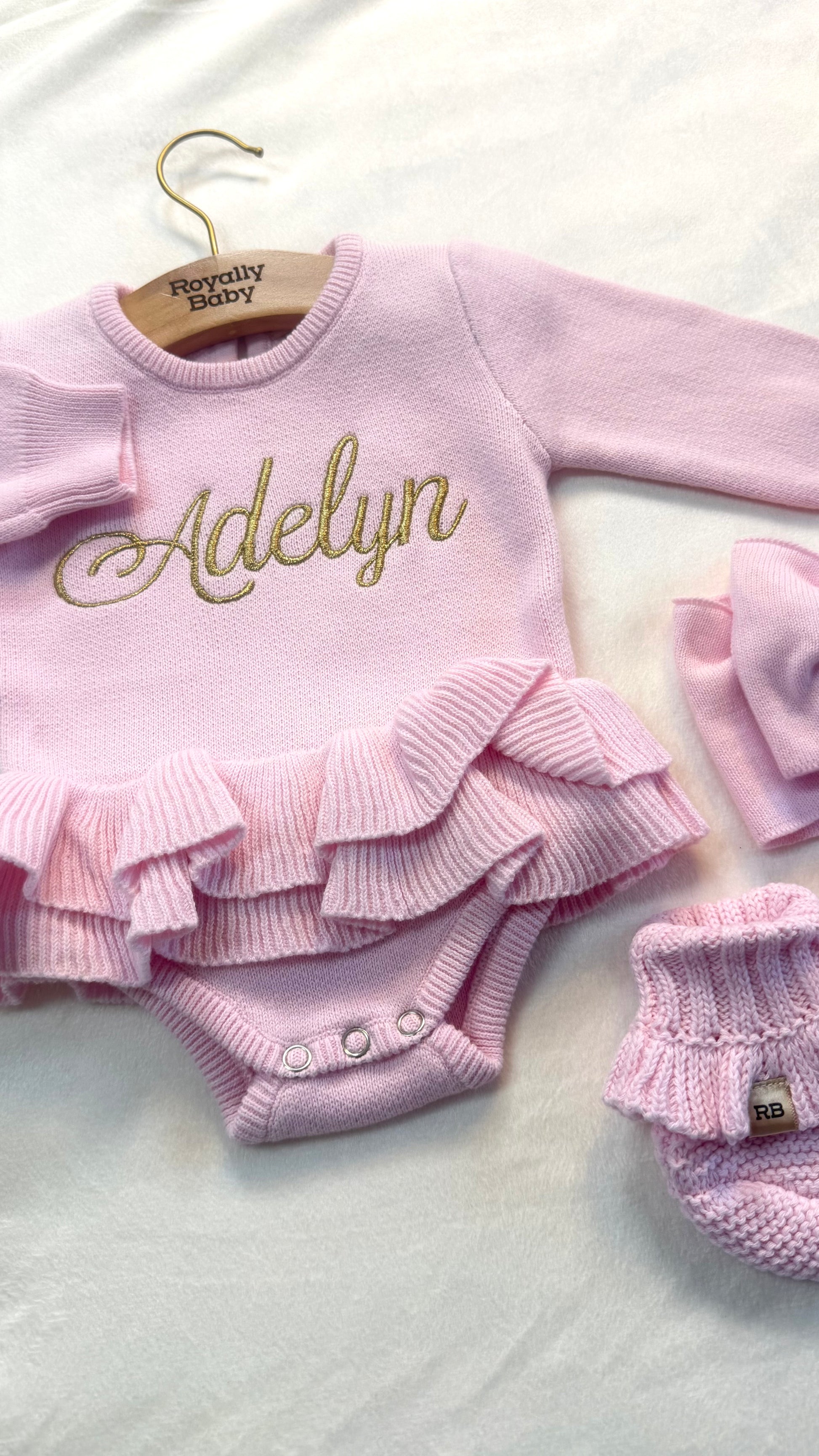 Personalized pink ballerina knit baby romper with ruffle detail and embroidered name, styled with matching booties for newborn coming home outfit