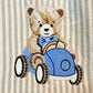 Vintage-style teddy bear embroidery driving a blue car on soft striped knit fabric for a personalized baby boy outfit or newborn keepsake clothing detail.