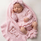 Newborn baby wearing personalized Petal Pink outfit set with embroidered name, including romper, bow, booties, and blanket