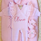 Personalized petal pink Butterfly long romper set displayed in a woven bassinet with matching bow and ruffle booties.