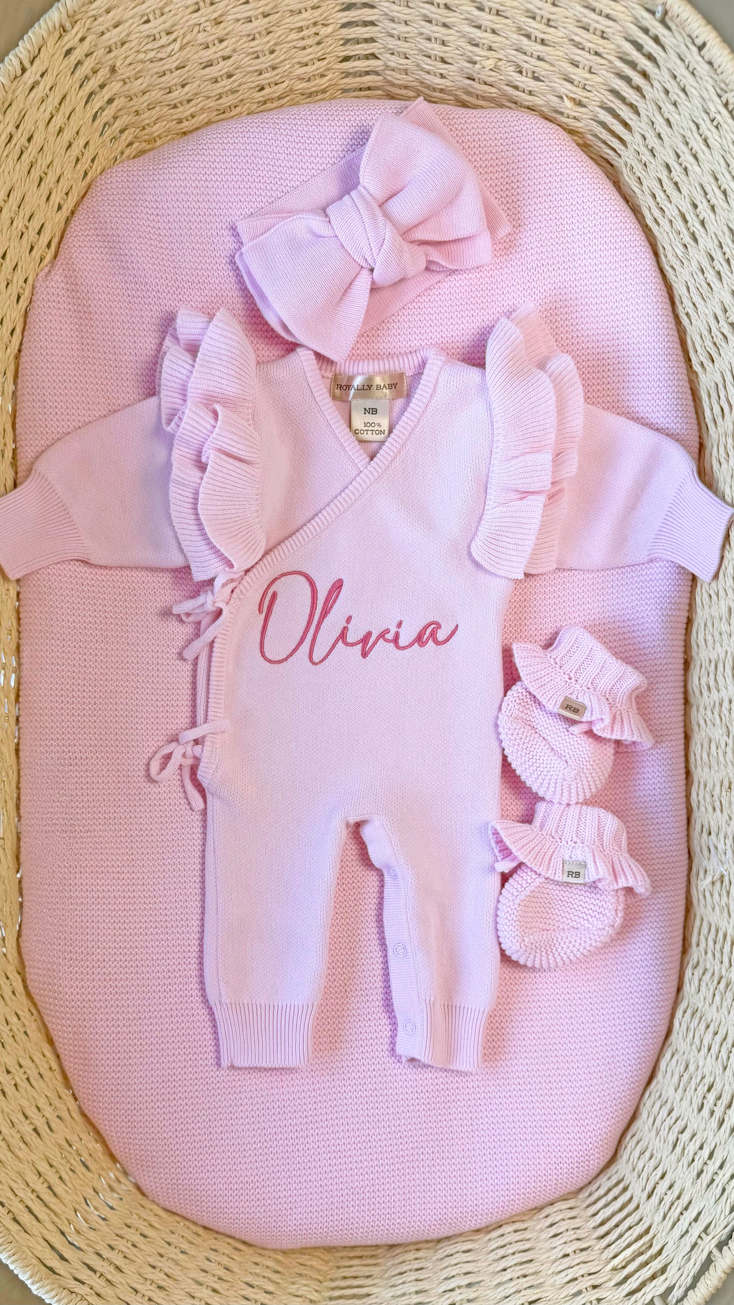Personalized petal pink Butterfly long romper set displayed in a woven bassinet with matching bow and ruffle booties.
