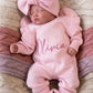 Sleeping newborn wearing the personalized Petal Pink Butterfly long romper with oversized bow and ruffle booties in a woven bassinet.