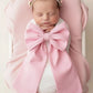 Swaddled newborn baby girl styled with an oversized pink bow sash and floral headband in a white bassinet for hospital announcement photos and luxury coming home photography.