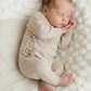 Newborn baby wearing classic knit wrap romper in soft khaki, lying on textured knit blanket