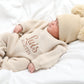 Newborn baby wearing classic knit wrap romper in soft khaki with personalized embroidery and knit hat