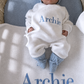 Overhead view of a newborn wearing the personalized Warm White and Baby Blue Kimono long romper set on a matching Archie knit blanket.