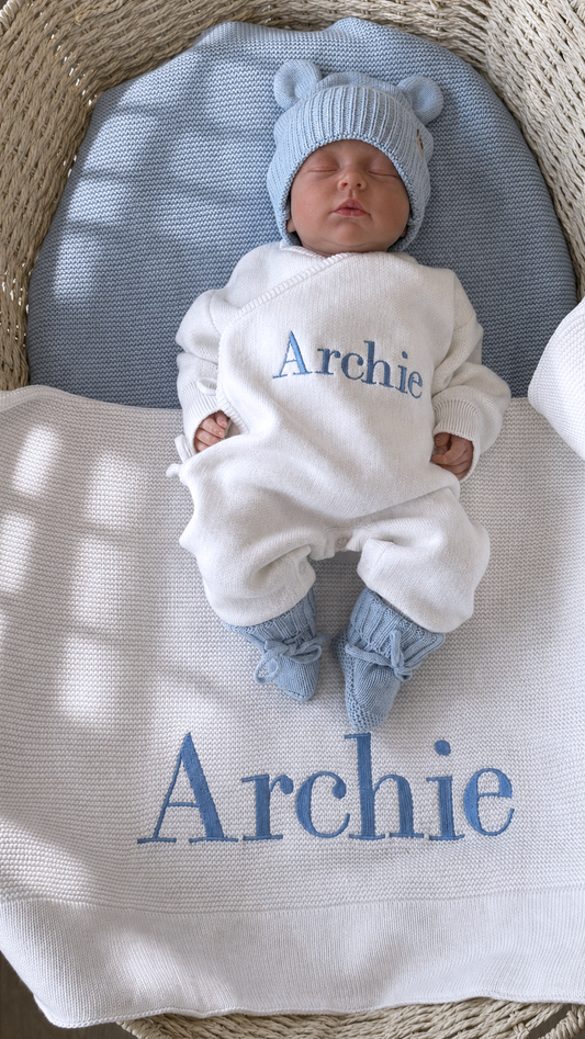Overhead view of a newborn wearing the personalized Warm White and Baby Blue Kimono long romper set on a matching Archie knit blanket.
