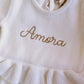 Amora embroidery on the Warm White Ballerina long romper with double ruffle waist and matching knit bow