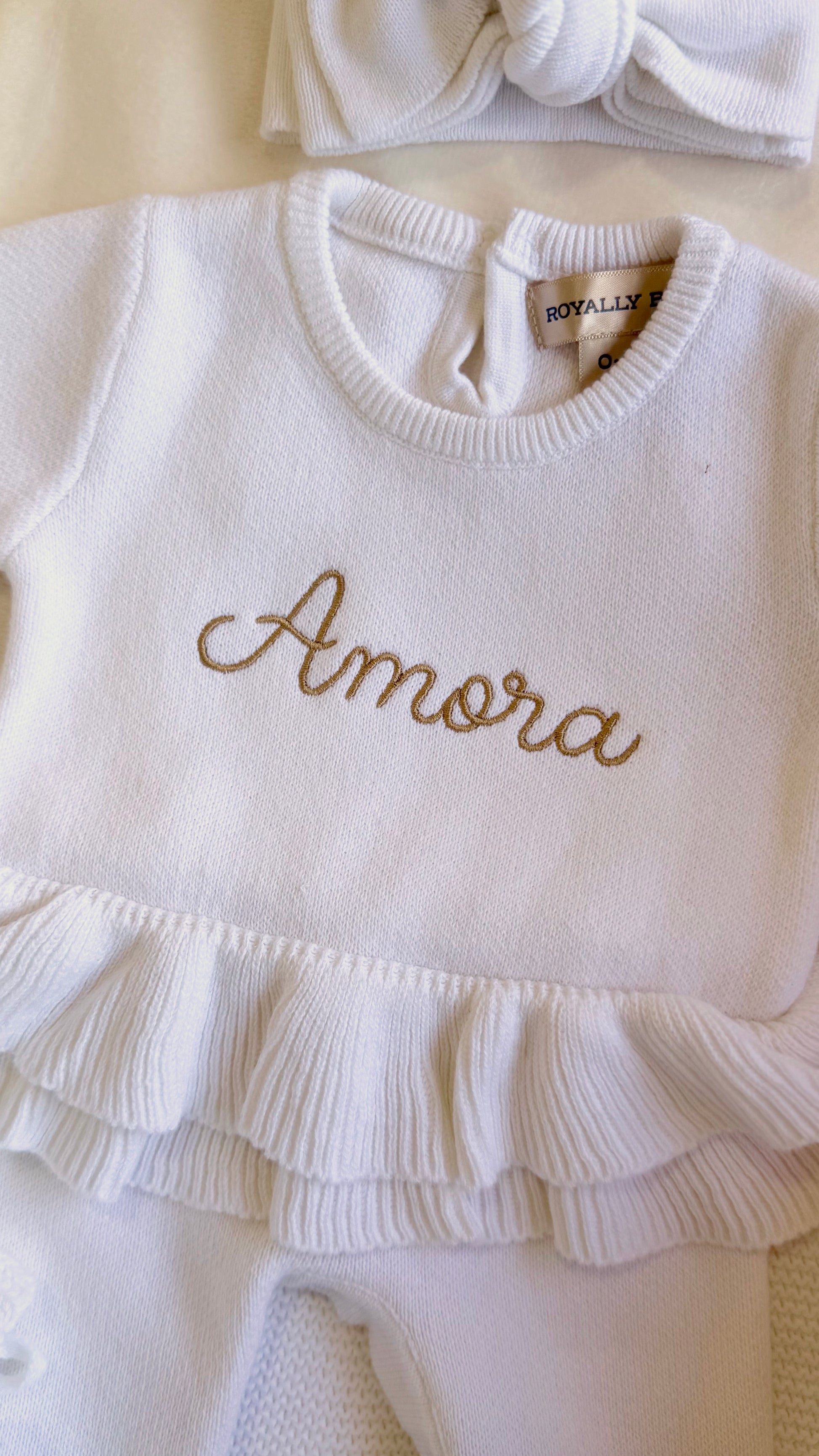 Amora embroidery on the Warm White Ballerina long romper with double ruffle waist and matching knit bow