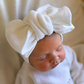 Close-up of a newborn wearing an oversized Warm White knit bow and personalized Ballerina long romper