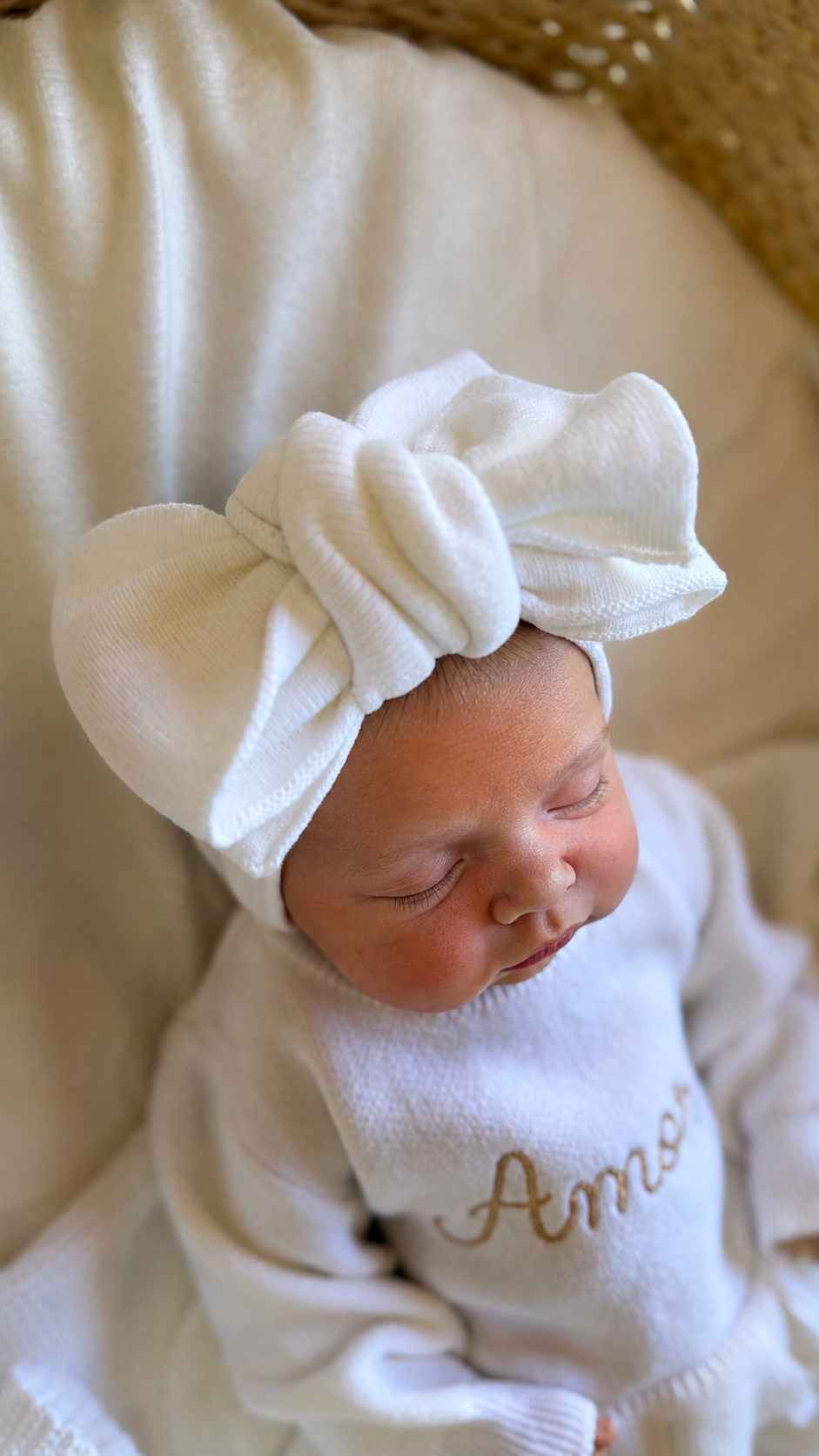 Close-up of a newborn wearing an oversized Warm White knit bow and personalized Ballerina long romper