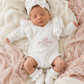 Newborn wearing personalized warm white Butterfly romper with bow and booties on textured pink blanket