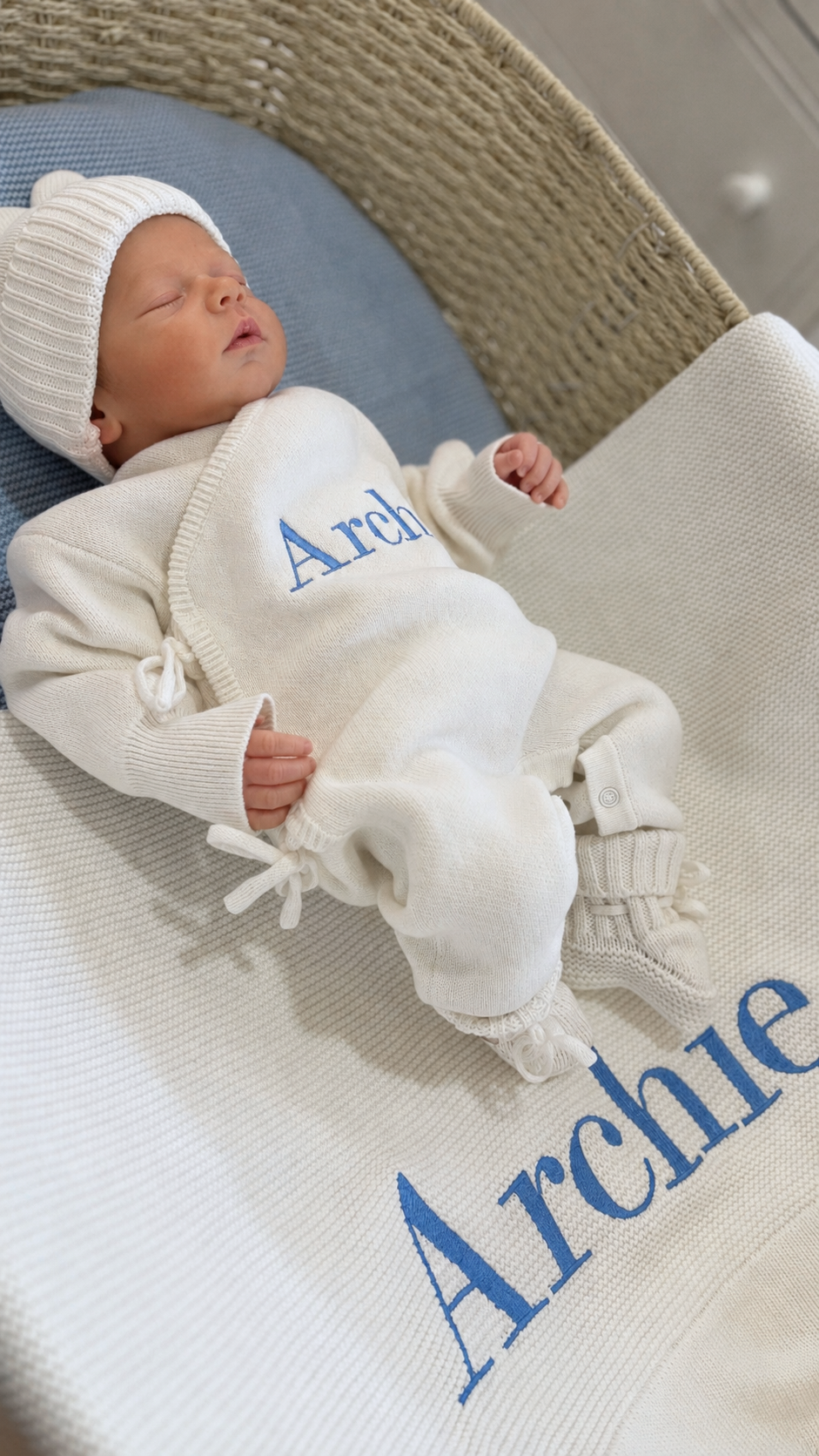 Newborn wearing the personalized Warm White Kimono long romper beside a matching embroidered knit blanket.