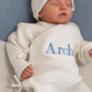 Newborn wearing the personalized Warm White Kimono long romper with matching bear-ear knit hat and classic newborn booties.