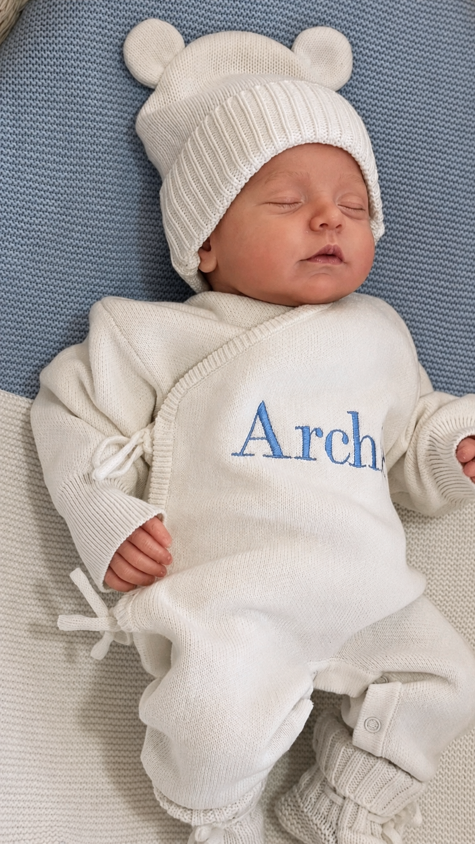 Newborn wearing the personalized Warm White Kimono long romper with matching bear-ear knit hat and classic newborn booties.