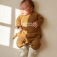 Baby wearing a personalized Teddy Brown knit romper while resting on a soft cream blanket
